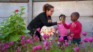 niñas y niños entre flores junto a una educadora de párvulos